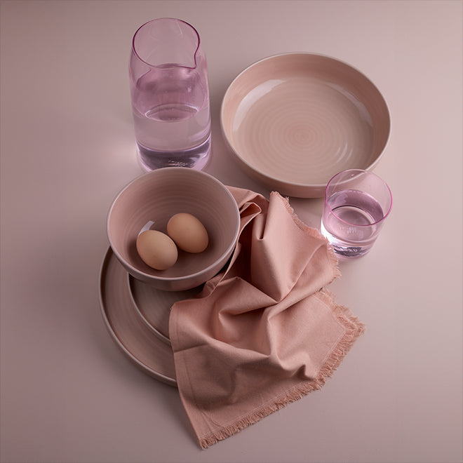 An arrangement of dinnerware, drinkware and table linens all in blush tones.